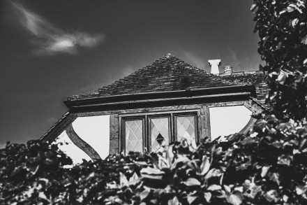 Black and white image of tudor-style property behind a hedge